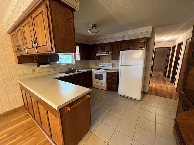 kitchen featuring white appliances, a sink, light countertops, a peninsula, and wallpapered walls