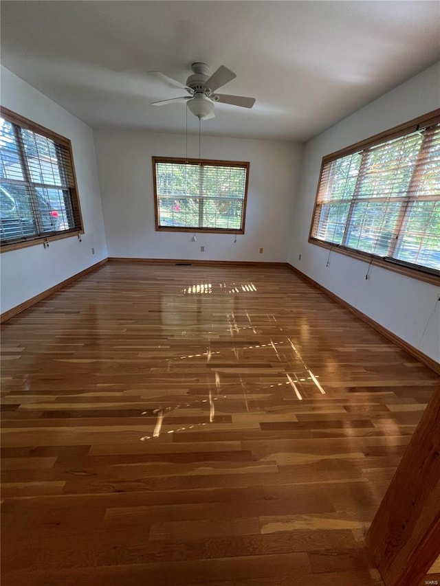 unfurnished room featuring wood finished floors, plenty of natural light, baseboards, and a ceiling fan