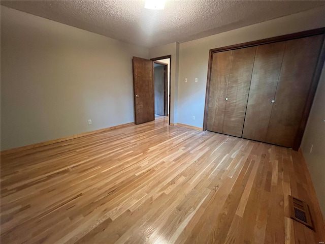 unfurnished bedroom featuring light wood-style floors, a textured ceiling, and a closet