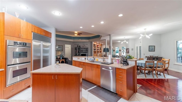 kitchen featuring appliances with stainless steel finishes, a kitchen island with sink, a sink, open floor plan, and a chandelier