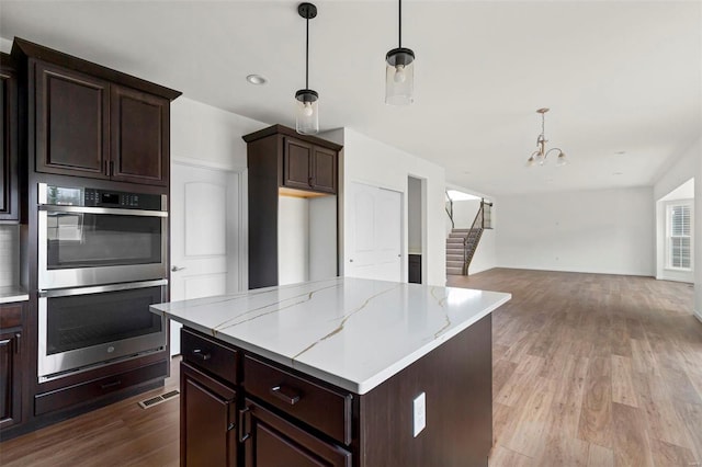 kitchen with stainless steel double oven, a chandelier, wood finished floors, hanging light fixtures, and dark brown cabinets