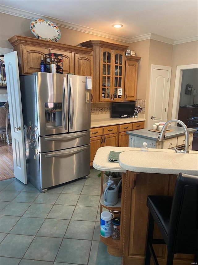 kitchen featuring stainless steel fridge with ice dispenser, light countertops, brown cabinetry, glass insert cabinets, and ornamental molding