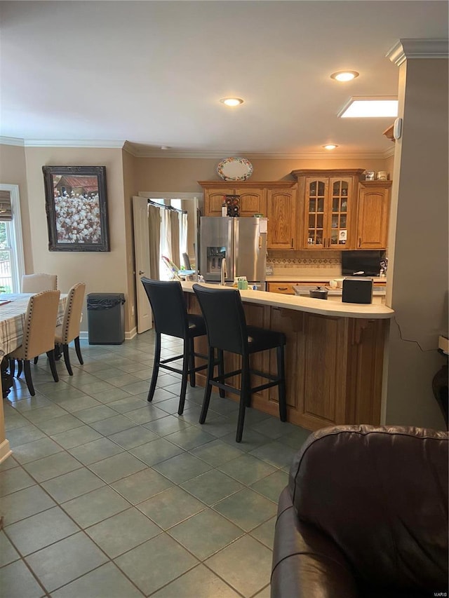 kitchen featuring stainless steel fridge with ice dispenser, brown cabinetry, glass insert cabinets, a peninsula, and ornamental molding