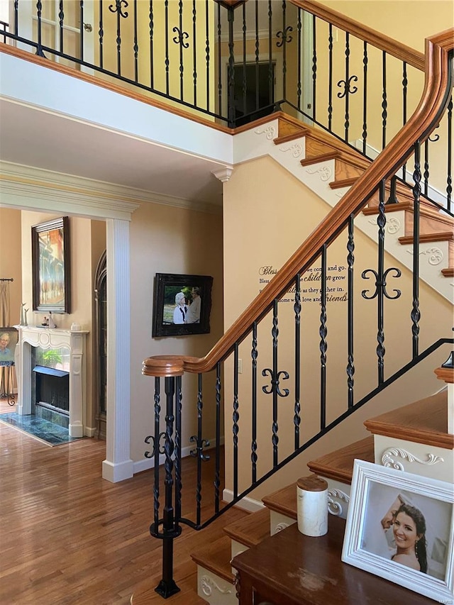 stairway with a fireplace, wood finished floors, crown molding, and baseboards
