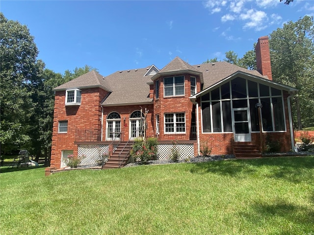 rear view of property featuring a chimney, brick siding, a sunroom, stairway, and a yard