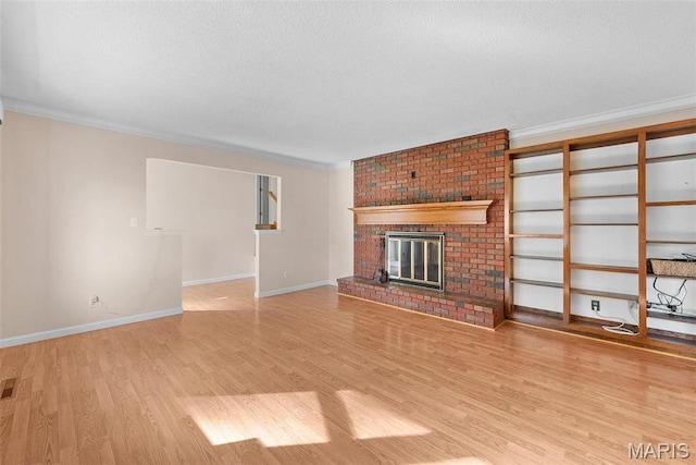 unfurnished living room with wood finished floors, crown molding, a brick fireplace, baseboards, and a textured ceiling