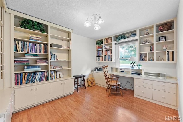 office featuring built in desk, light wood-type flooring, a textured ceiling, and a chandelier