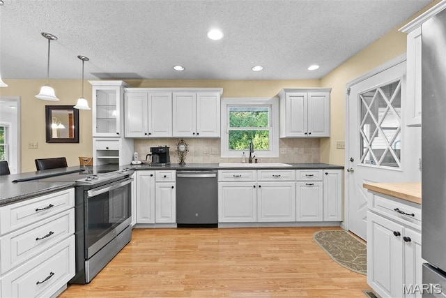 kitchen with stainless steel appliances, a sink, a textured ceiling, dark countertops, and decorative backsplash