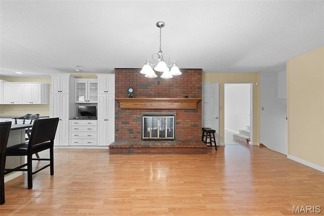 living room featuring light wood finished floors, a chandelier, baseboards, a fireplace, and a textured ceiling