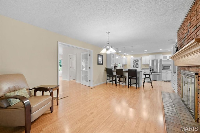 dining room with a fireplace, light wood-style flooring, a chandelier, a textured ceiling, and baseboards