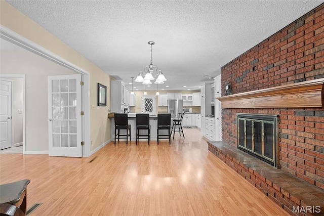 dining space featuring a chandelier, light wood-type flooring, a fireplace, a textured ceiling, and baseboards
