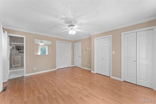 unfurnished bedroom featuring two closets, a textured ceiling, light wood finished floors, crown molding, and baseboards