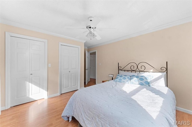 bedroom featuring light wood-style floors, ornamental molding, two closets, baseboards, and ceiling fan
