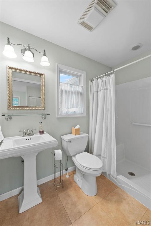 bathroom with toilet, a shower stall, tile patterned flooring, and baseboards