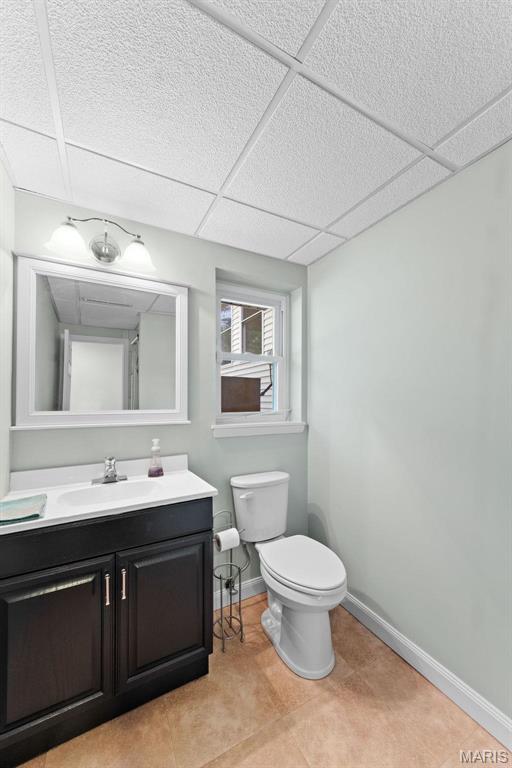 bathroom featuring a paneled ceiling, toilet, baseboards, and vanity