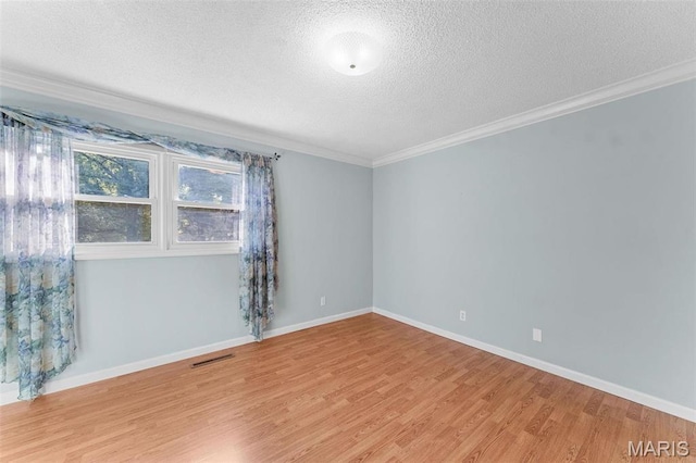 spare room featuring a textured ceiling, crown molding, wood finished floors, and baseboards