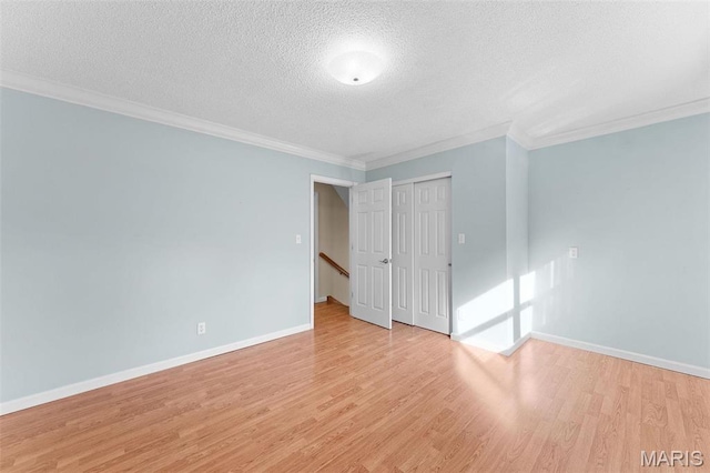 unfurnished bedroom featuring a textured ceiling, light wood-type flooring, crown molding, baseboards, and a closet