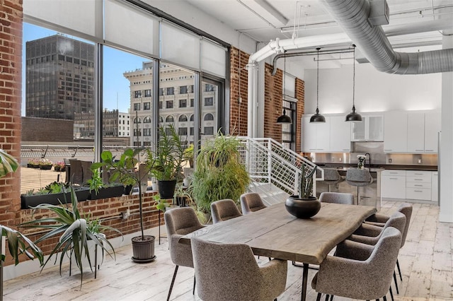 dining room with brick wall, a high ceiling, a city view, and light wood finished floors