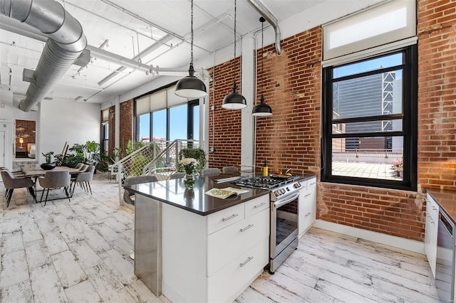 kitchen with stainless steel gas stove, dark countertops, brick wall, light wood-style flooring, and baseboards
