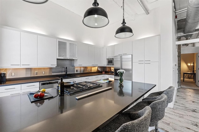 kitchen featuring built in appliances, a sink, dark countertops, a breakfast bar area, and a towering ceiling