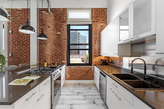 kitchen featuring stainless steel appliances, a sink, brick wall, dark countertops, and white cabinets
