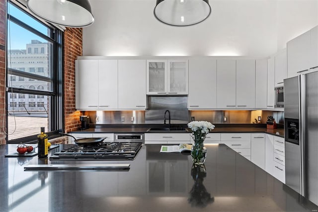 kitchen featuring stainless steel refrigerator with ice dispenser, dark countertops, a sink, white cabinets, and gas stovetop
