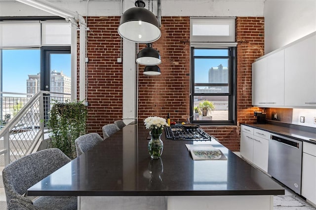 kitchen with dishwasher, dark countertops, brick wall, white cabinets, and a kitchen island