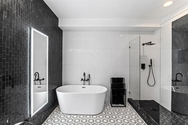 bathroom with tile walls, a walk in shower, a freestanding tub, and tile patterned floors