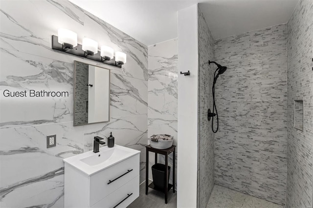 bathroom featuring tiled shower, vanity, and tile walls