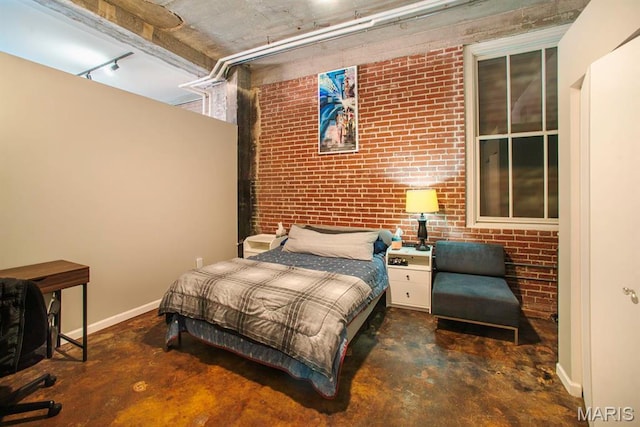 bedroom featuring concrete flooring, brick wall, baseboards, and track lighting