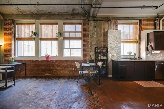 kitchen with stainless steel dishwasher, brick wall, a sink, and light countertops
