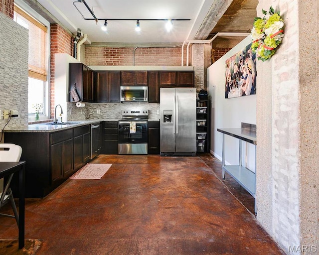 kitchen featuring stainless steel appliances, a sink, dark brown cabinets, finished concrete floors, and light stone counters