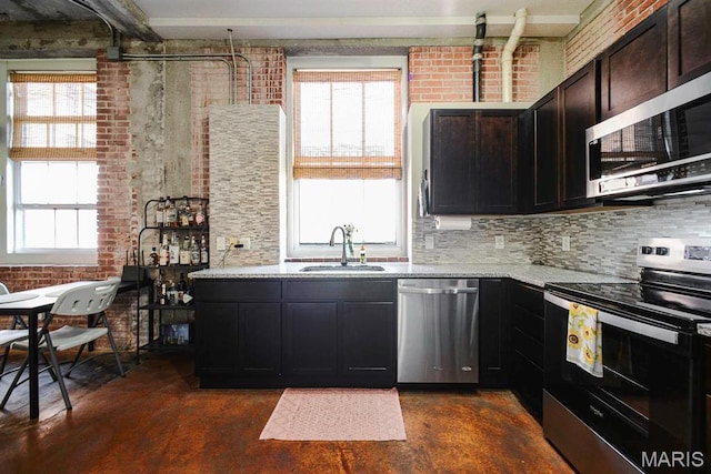 kitchen with appliances with stainless steel finishes, a sink, finished concrete flooring, healthy amount of natural light, and brick wall