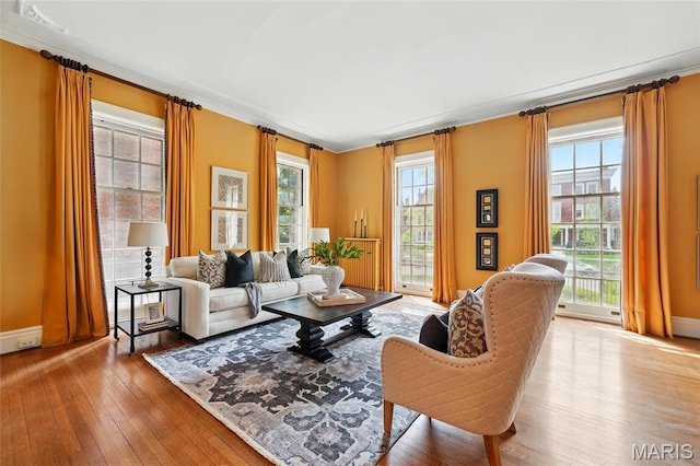 living area featuring healthy amount of natural light, hardwood / wood-style floors, baseboards, and crown molding