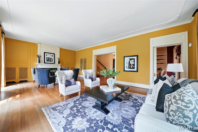living room featuring wood-type flooring, a fireplace, stairs, crown molding, and baseboards