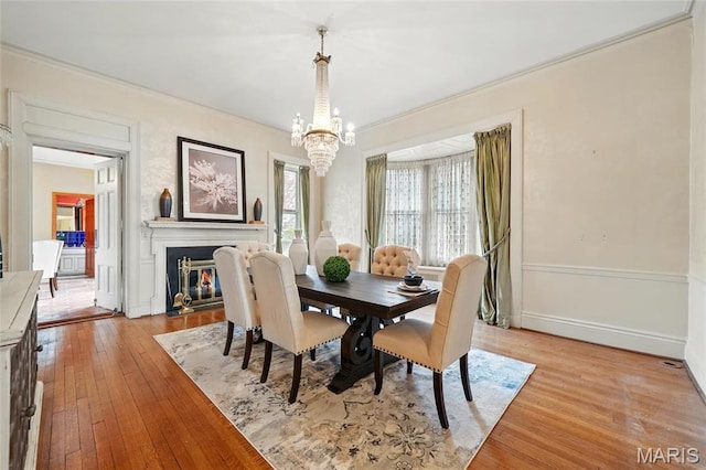 dining room featuring a chandelier, light wood finished floors, crown molding, a fireplace with flush hearth, and baseboards