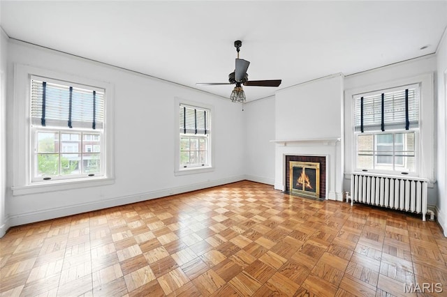 unfurnished living room with radiator heating unit, baseboards, a fireplace, and ceiling fan
