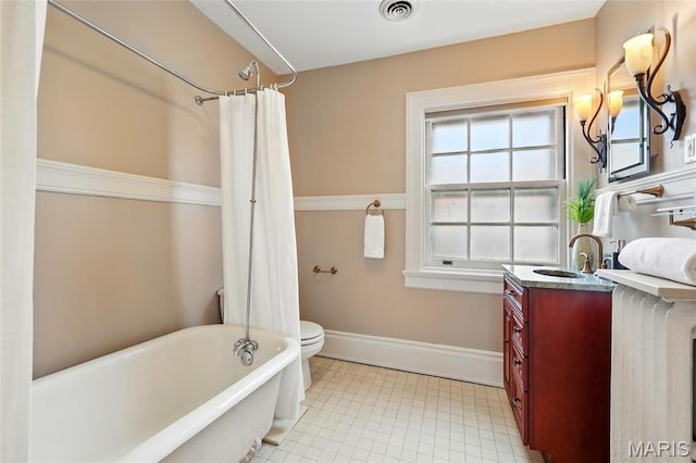 full bathroom with a freestanding tub, vanity, toilet, baseboards, and tile patterned floors