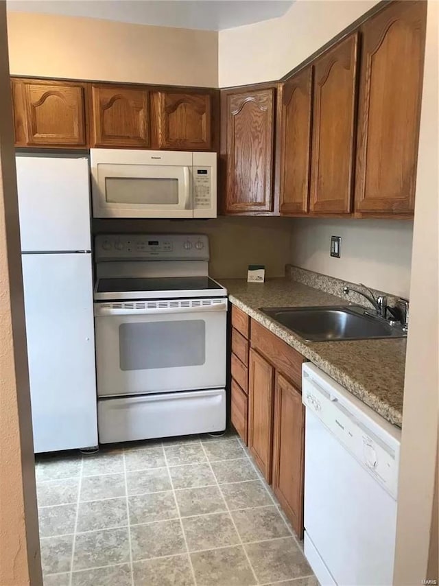 kitchen with white appliances, a sink, and brown cabinetry