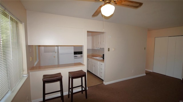 kitchen with white cabinetry, ceiling fan, carpet flooring, light countertops, and a kitchen bar