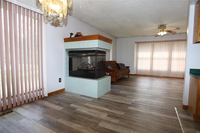 living area with ceiling fan, baseboards, dark wood-style flooring, a tile fireplace, and a chandelier