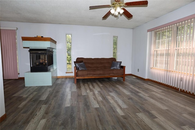 sitting room featuring a ceiling fan, a textured ceiling, wood finished floors, a tiled fireplace, and baseboards