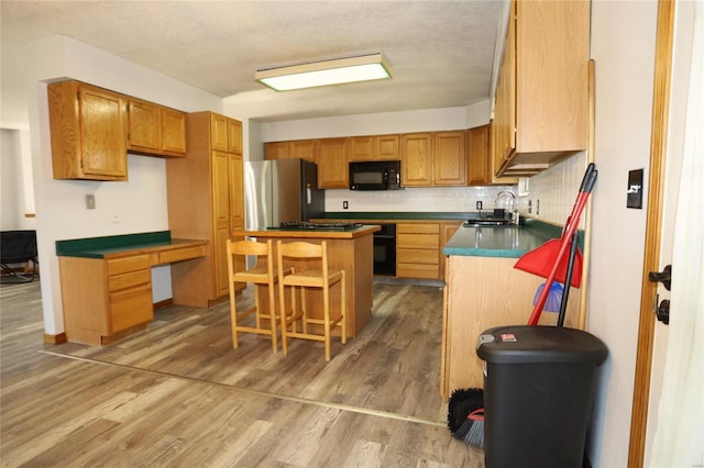 kitchen with black appliances, a sink, a kitchen island, a breakfast bar, and backsplash