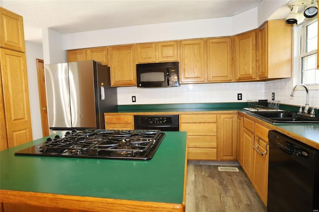 kitchen with black appliances, a sink, wood finished floors, tasteful backsplash, and dark countertops