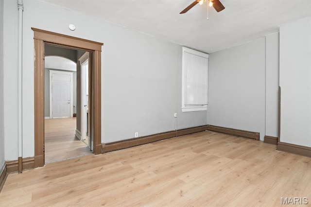 spare room featuring arched walkways, a ceiling fan, light wood-type flooring, and baseboards