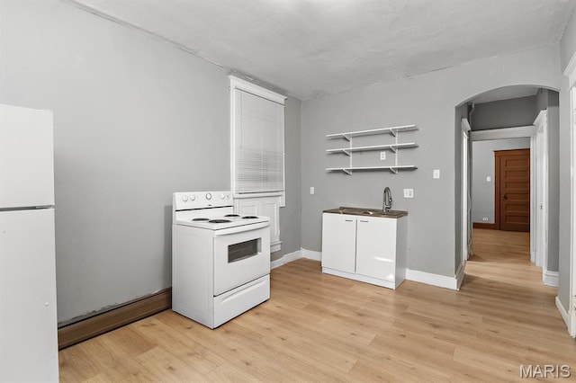 kitchen featuring white appliances, arched walkways, light wood finished floors, and baseboards