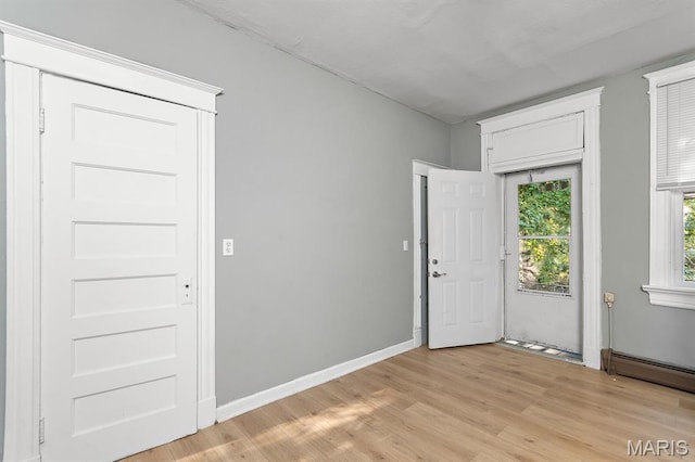 foyer entrance featuring a baseboard heating unit and light wood-style floors
