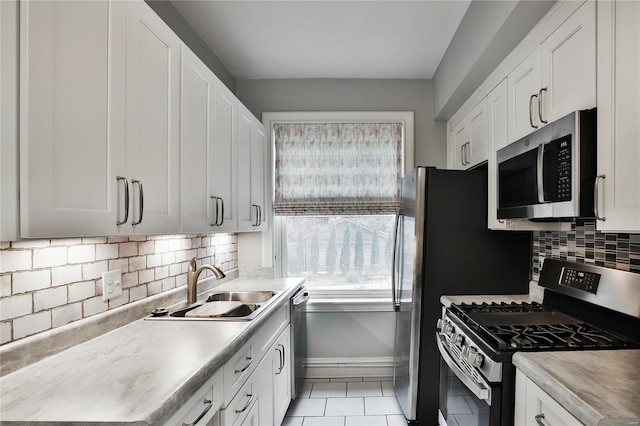 kitchen with appliances with stainless steel finishes, a sink, light tile patterned floors, backsplash, and white cabinetry