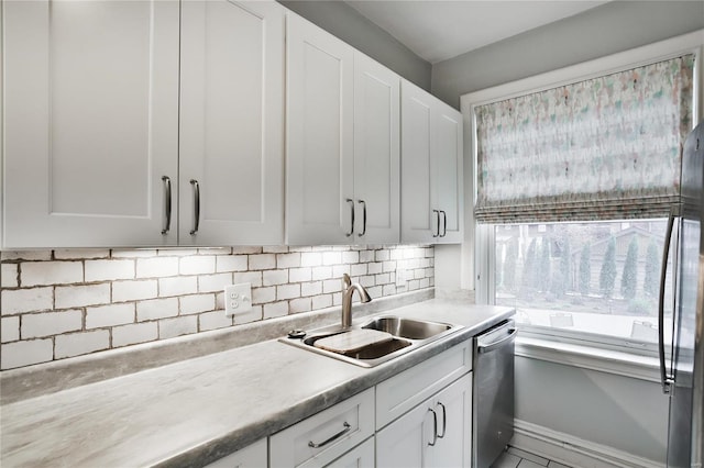 kitchen with appliances with stainless steel finishes, backsplash, white cabinetry, a sink, and light countertops