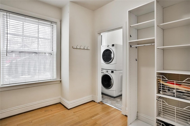 laundry area featuring stacked washer / dryer, light wood-type flooring, plenty of natural light, and baseboards